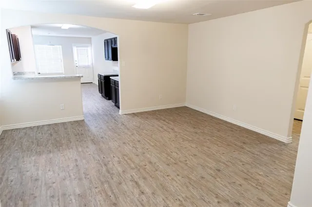 an empty room with wooden floor and kitchen view