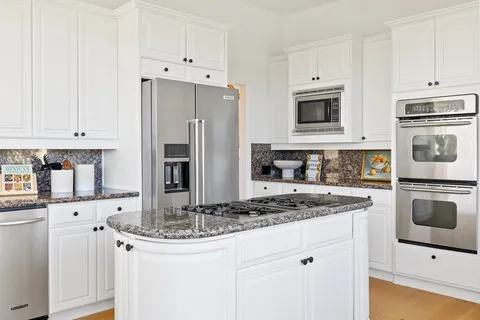 a kitchen with stainless steel appliances granite countertop a refrigerator stove and white cabinets