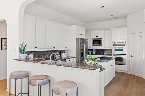 a kitchen with stainless steel appliances a sink a stove a refrigerator cabinets and chairs