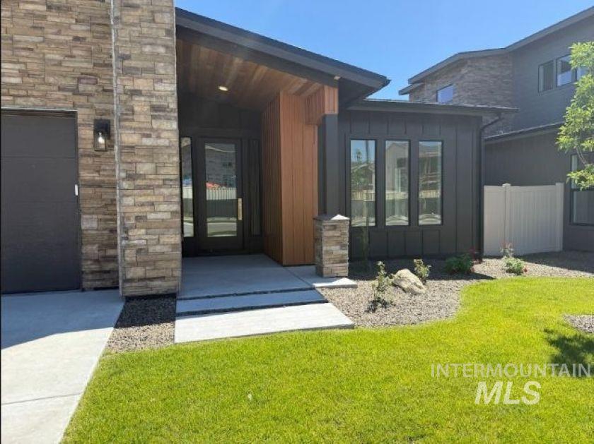 683 West Wrangler Street Meridian, ID 83646 - Photo 2 of 23 Contemporary exterior featuring stone veneer, dark siding, wood paneling, a large glass entry door, and a dark garage door