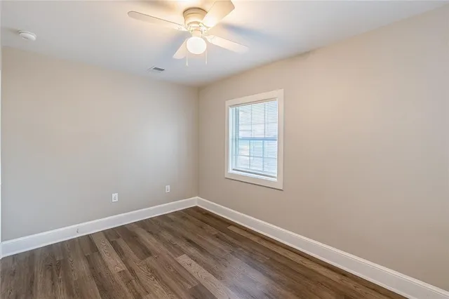 an empty room with wooden floor fan and windows