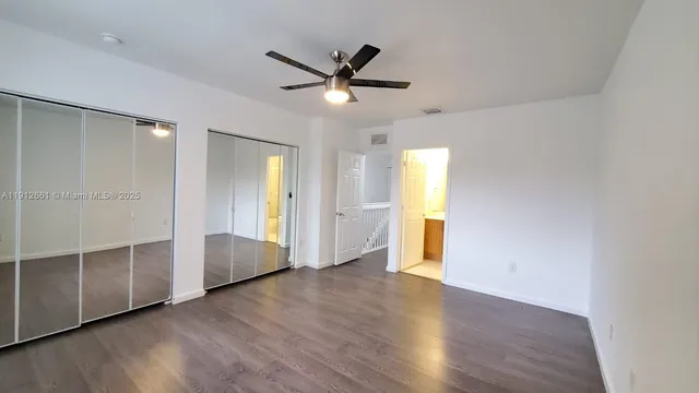 an empty room with wooden floor ceiling fan and windows