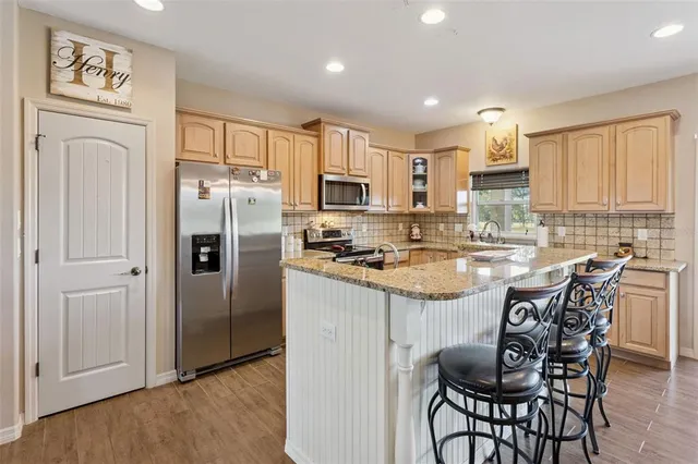 a kitchen with stainless steel appliances granite countertop a refrigerator a stove a sink and a dining table with wooden cabinet