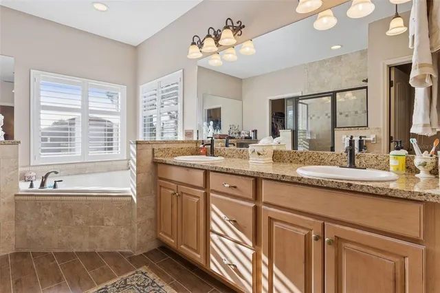 a bathroom with a granite countertop sink a large mirror a bathtub and next to a window