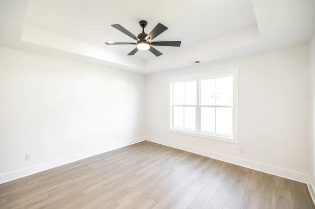 an empty room with wooden floor fan and windows