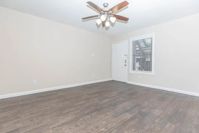 an empty room with wooden floor fan and windows