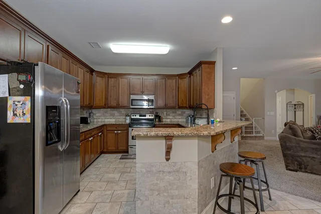 a kitchen with stainless steel appliances granite countertop a refrigerator a stove a sink a dining table and chairs