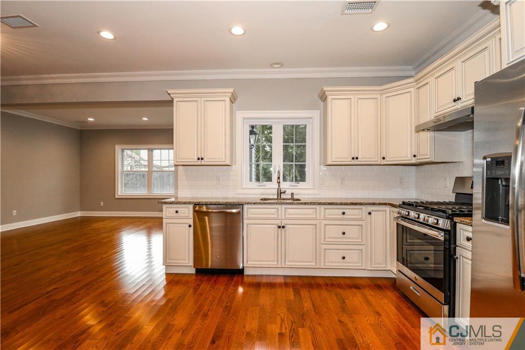 32 Windsor Road Edison, NJ 08817 - Photo 11 of 24 a large kitchen with granite countertop a stove top oven a sink dishwasher and white cabinets with wooden floor