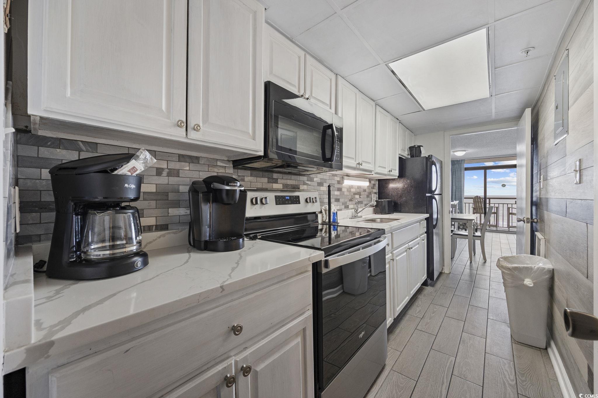 1501 South Ocean Boulevard, Unit 338 Myrtle Beach, SC 29577 - Photo 14 of 40 Kitchen featuring black appliances, white cabinetry, backsplash, light stone countertops, and a paneled ceiling