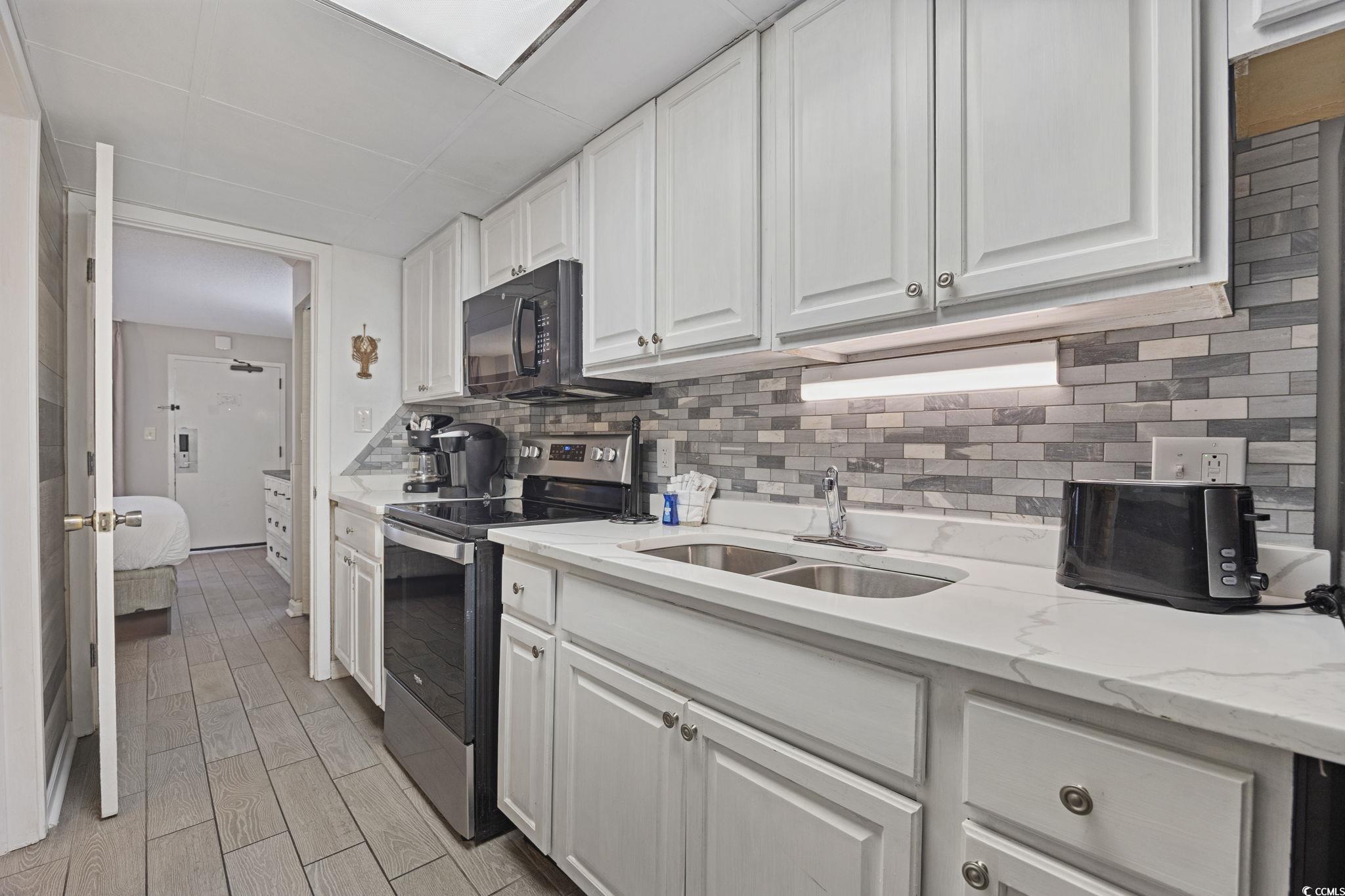 1501 South Ocean Boulevard, Unit 338 Myrtle Beach, SC 29577 - Photo 15 of 40 Kitchen featuring electric range, decorative backsplash, white cabinets, light stone counters, and black microwave