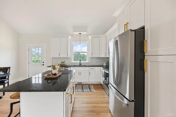 a kitchen with granite countertop a refrigerator a sink a stove and white cabinets