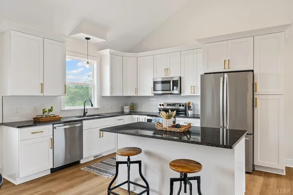 a kitchen with stainless steel appliances granite countertop a refrigerator a stove a sink dishwasher and white cabinets with wooden floor