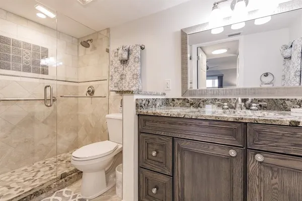 a bathroom with a granite countertop sink a toilet a mirror and shower
