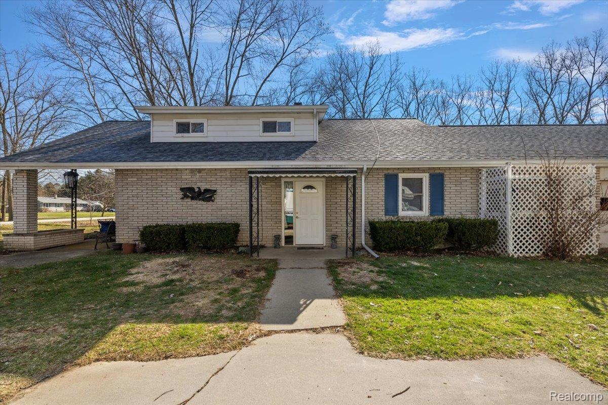 View of front of property with a front yard, a shingled roof, and brick siding