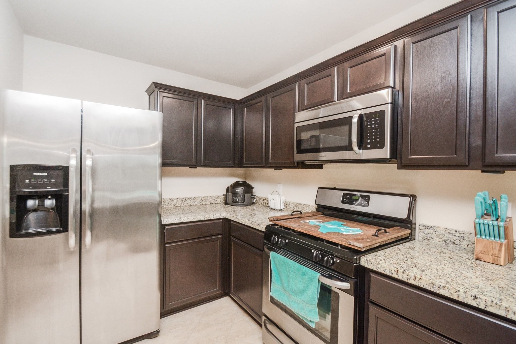 23318 Dukes Run Drive Spring, TX 77373 - Photo 11 of 41 This modern kitchen features dark wood cabinets, granite countertops, and stainless steel appliances, including a double-door fridge and a built-in microwave. It has a cozy, efficient layout with tiled flooring.