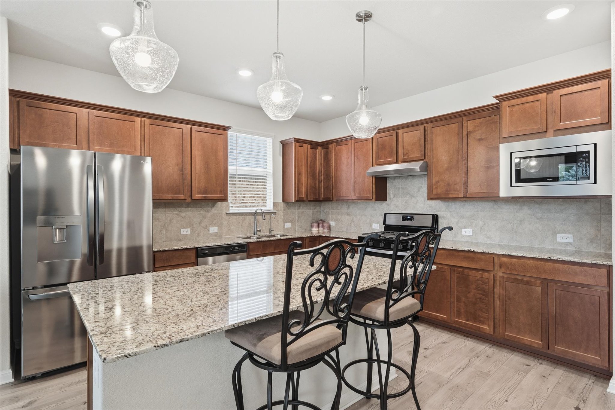 113 Lafayette Street Georgetown, TX 78633 - Photo 12 of 39 Open-concept kitchen featuring an island with a light-toned countertop, wood-finish flooring, stainless steel appliances, abundant cabinetry, and pendant lighting