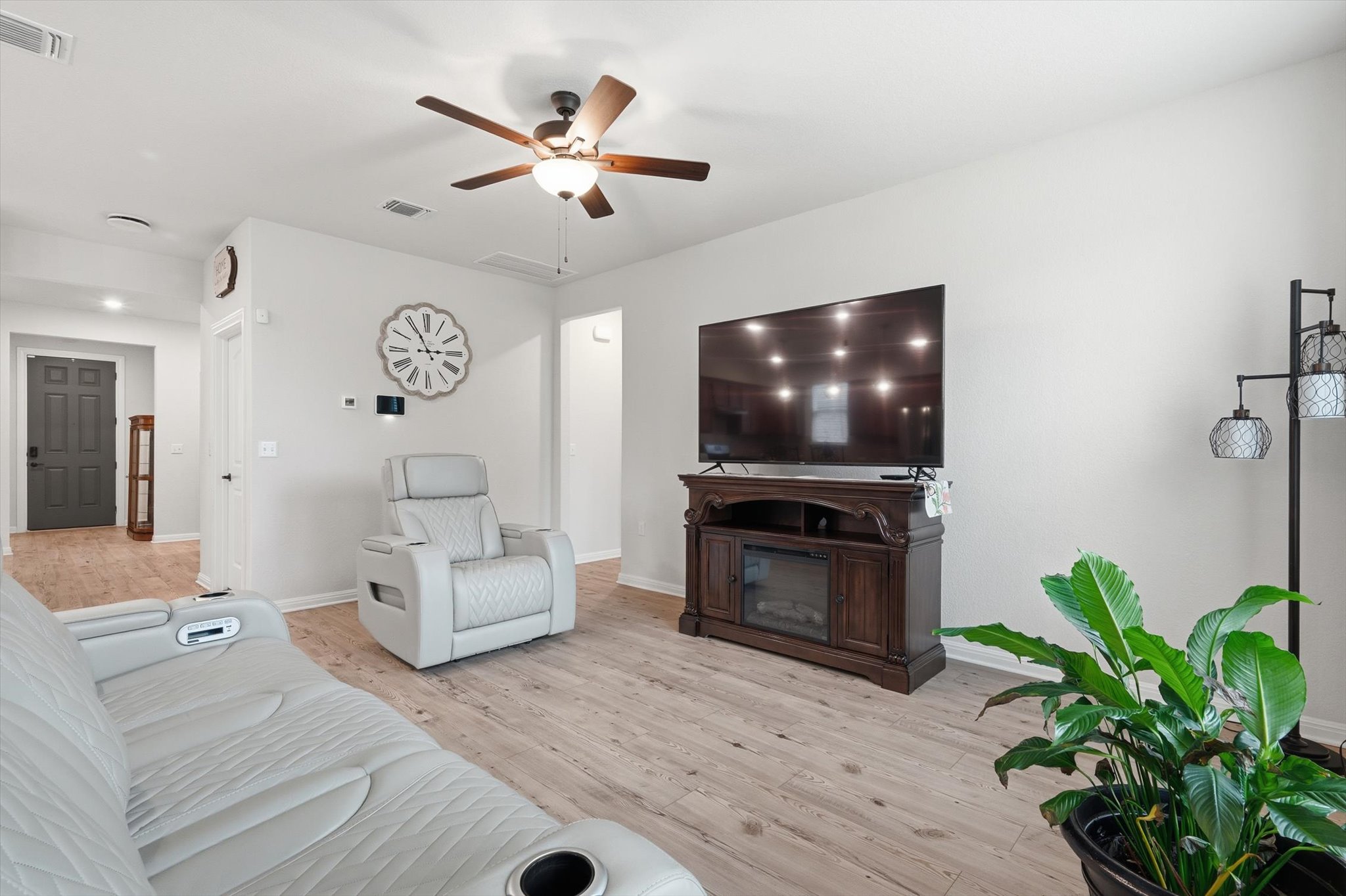 113 Lafayette Street Georgetown, TX 78633 - Photo 17 of 39 Open-concept living space with light-toned wood-finish flooring, a ceiling fan with integrated lighting, and a dark wood media console featuring an electric fireplace insert