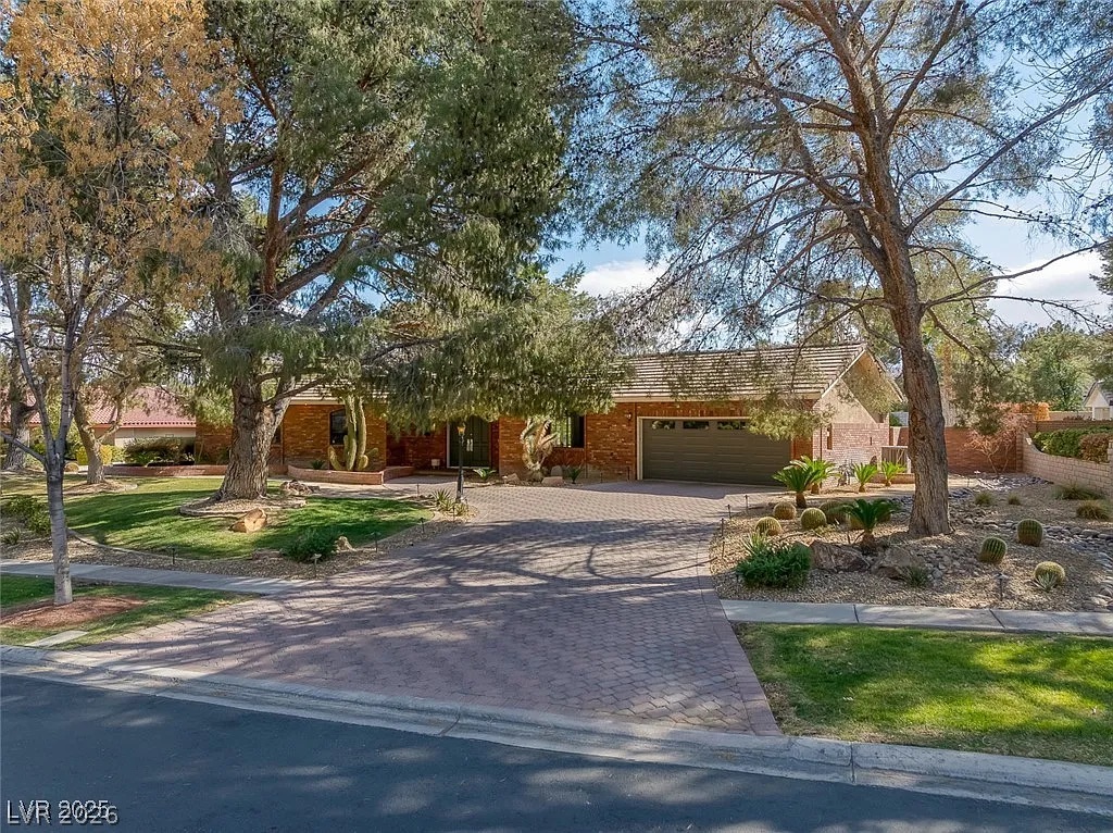 9 Quail Run Road Henderson, NV 89014 - Photo 3 of 57 Mature trees frame this brick residence with a paved driveway and desert-inspired landscaping.