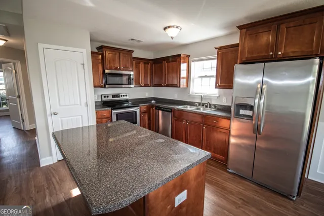 a kitchen with granite countertop stainless steel appliances a refrigerator a stove a sink a center island and wooden floor