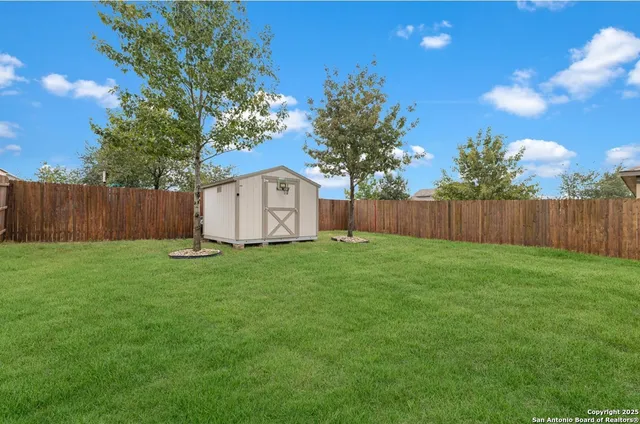 a view of a backyard with large trees and wooden fence