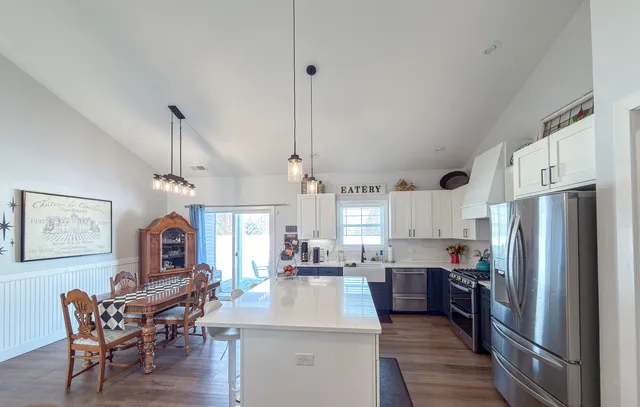 a kitchen with stainless steel appliances granite countertop a refrigerator a sink dishwasher a dining table and chairs with wooden floor