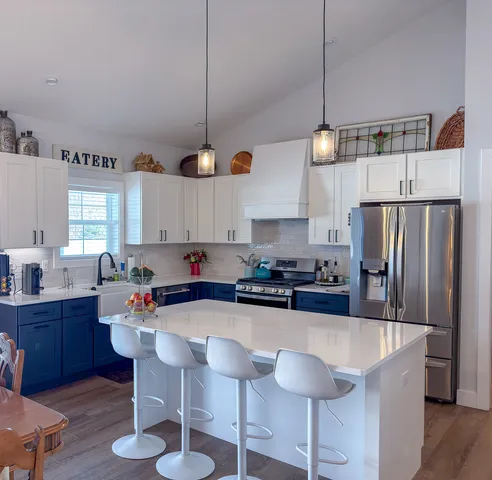 a kitchen with stainless steel appliances granite countertop a refrigerator a stove a sink a dining table and chairs with wooden floor