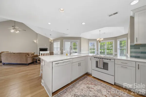 a large white kitchen with a sink and dishwasher a stove top oven with wooden floor