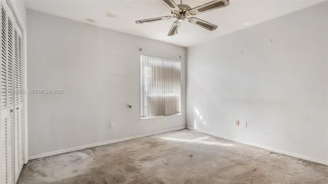 an empty room with a chandelier fan and windows