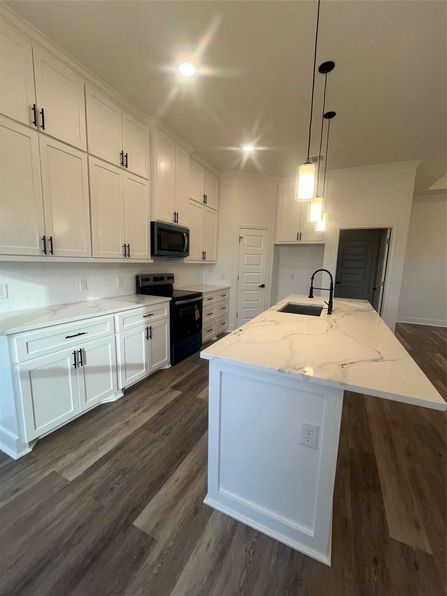 33416 FM 521 Road Angleton, TX 77515 - Photo 9 of 21 This modern kitchen features sleek white cabinetry, a large Quartz-patterned island with a built-in sink, black & stainless steel appliances, and elegant pendant lighting, all set on stylish medium gray/wood water proof plank flooring.