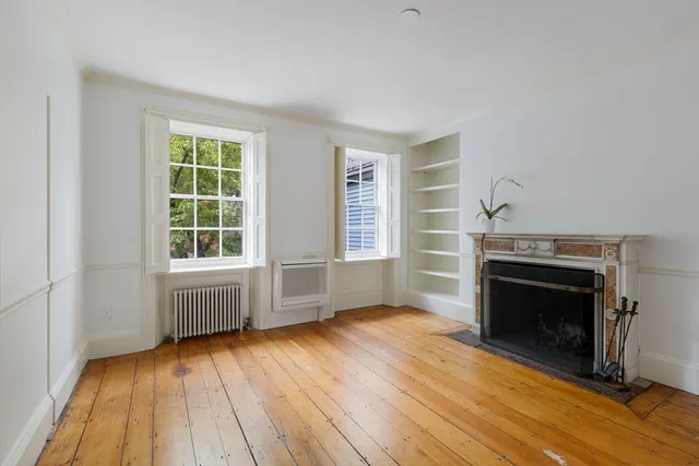 an empty room with wooden floor fireplace and windows