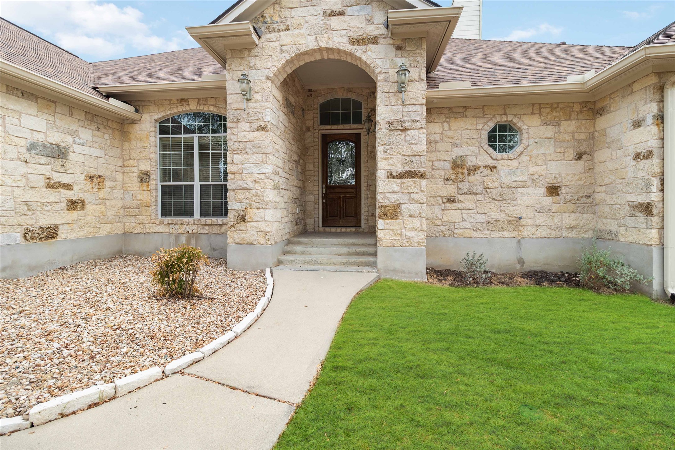 Entrance to property featuring stone siding, roof with shingles, and a lawn