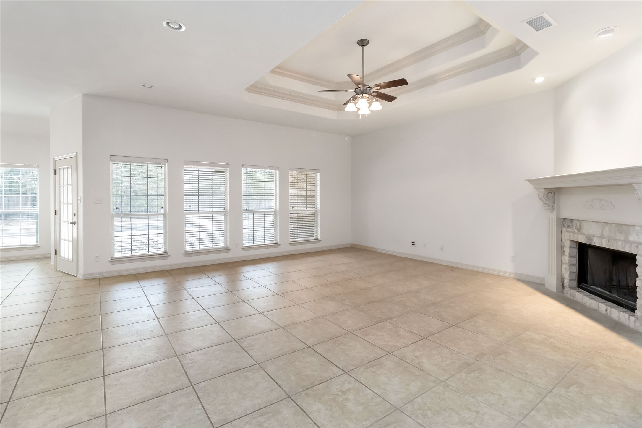 167 Winchester Road Bastrop, TX 78602 - Photo 11 of 34 Unfurnished living room with a raised ceiling, light tile patterned flooring, a tiled fireplace, ceiling fan, and recessed lighting