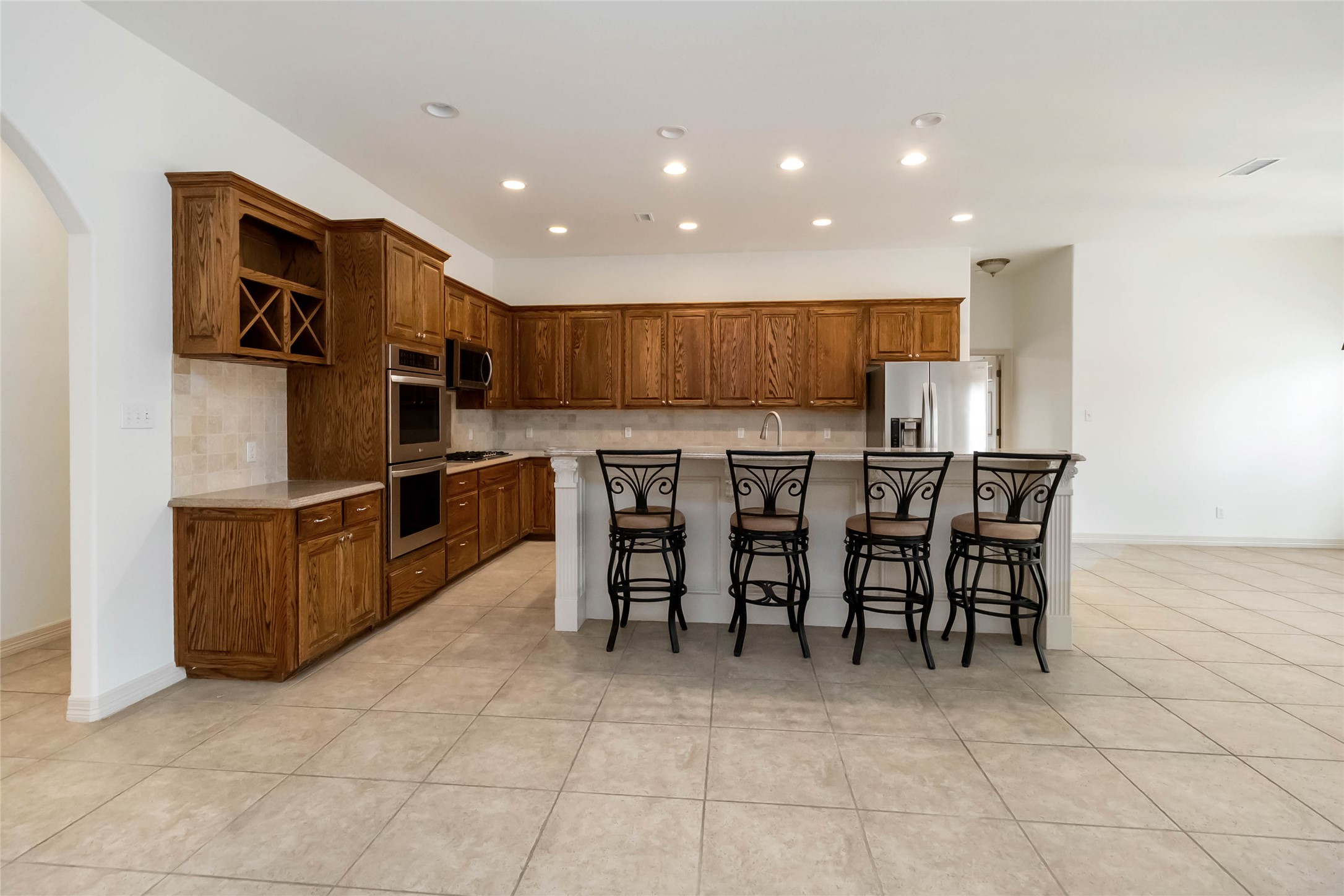 167 Winchester Road Bastrop, TX 78602 - Photo 13 of 34 Kitchen with a kitchen breakfast bar, a kitchen island, decorative backsplash, brown cabinetry, and arched walkways