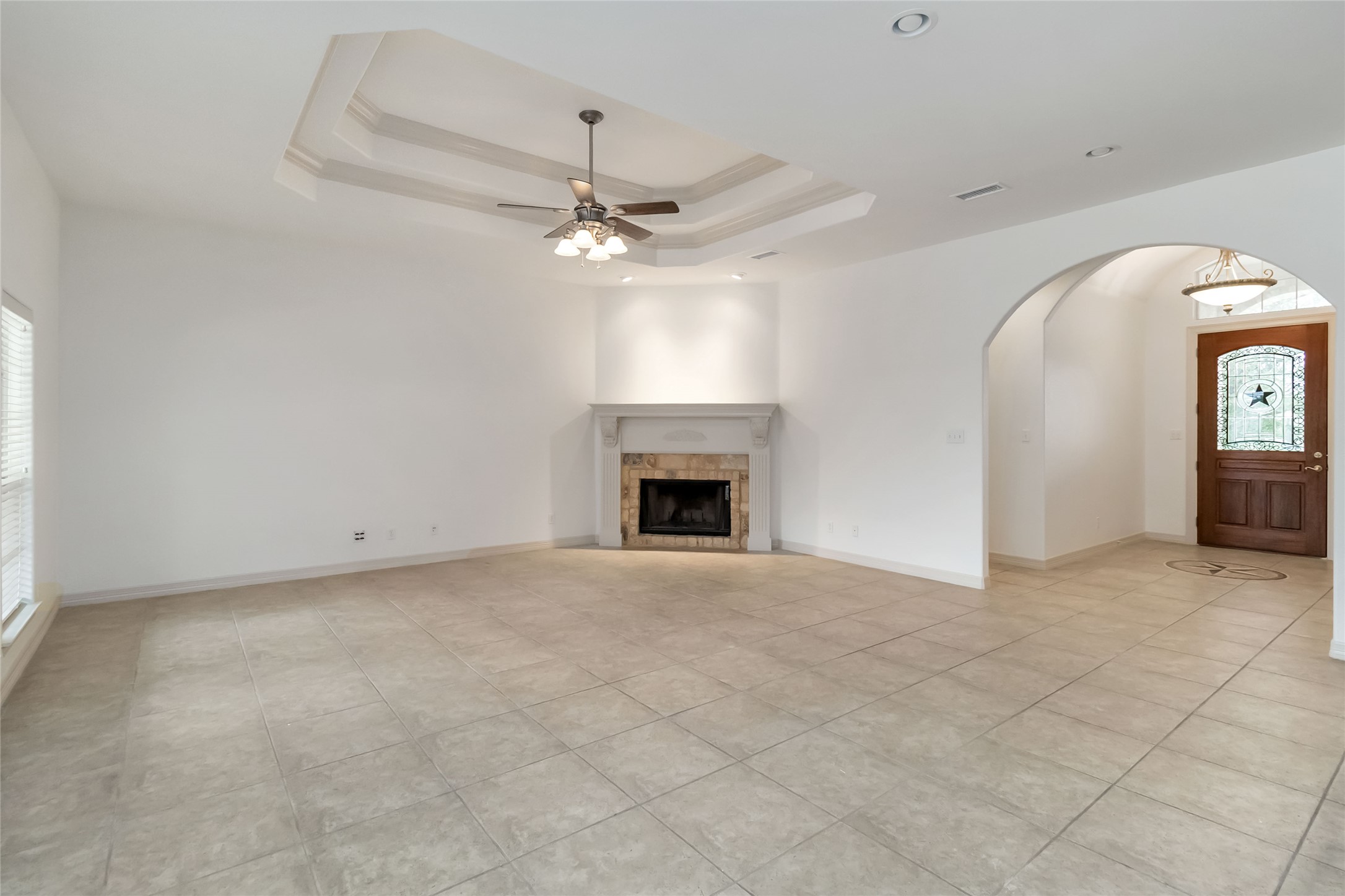 167 Winchester Road Bastrop, TX 78602 - Photo 10 of 34 Unfurnished living room featuring a raised ceiling, a tile fireplace, ceiling fan, crown molding, and light tile patterned floors