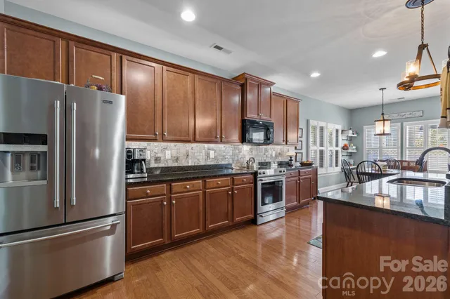 a kitchen with stainless steel appliances granite countertop a refrigerator a sink dishwasher a stove with wooden cabinets and floor