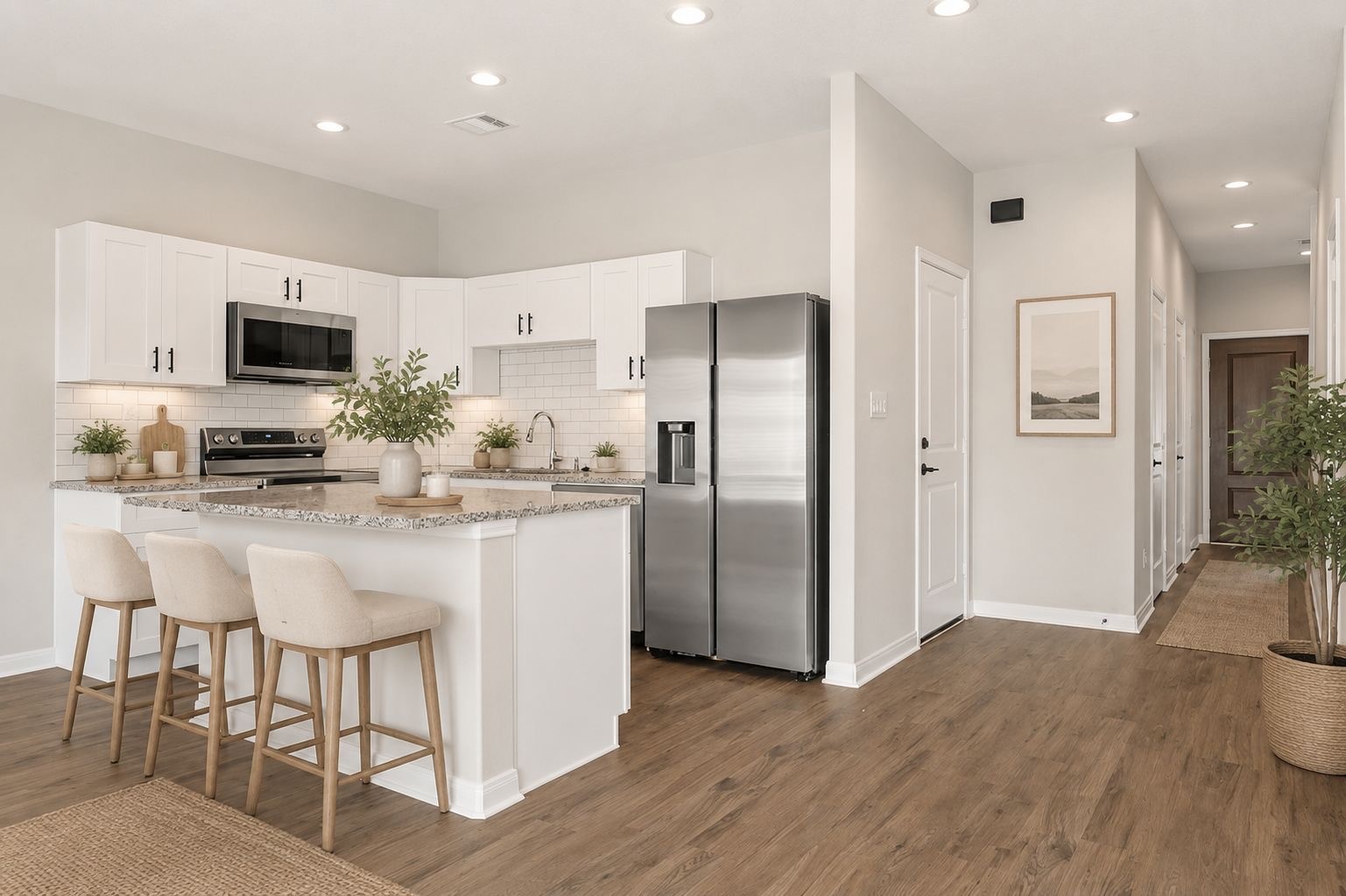Modern kitchen with white cabinetry, stainless steel appliances, granite countertops, and subway tile backsplash. Features wood flooring and ample natural light.