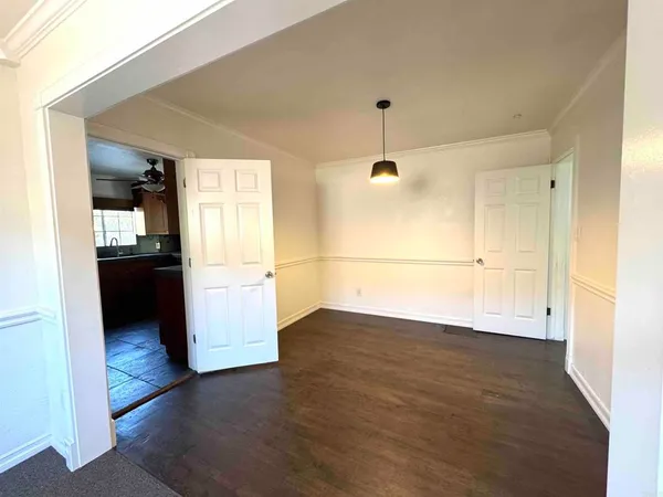 an empty room with wooden floor and kitchen view