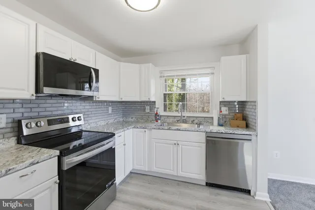a kitchen with granite countertop white cabinets sink and stainless steel appliances