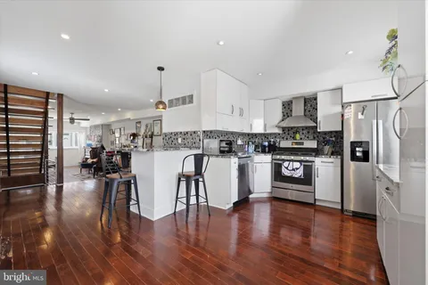 a kitchen with stainless steel appliances granite countertop a refrigerator a stove top oven a sink dishwasher and white cabinets with wooden floor