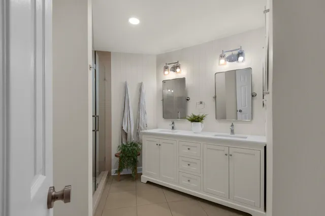 a spacious bathroom with a double vanity sink a large mirror a shower and