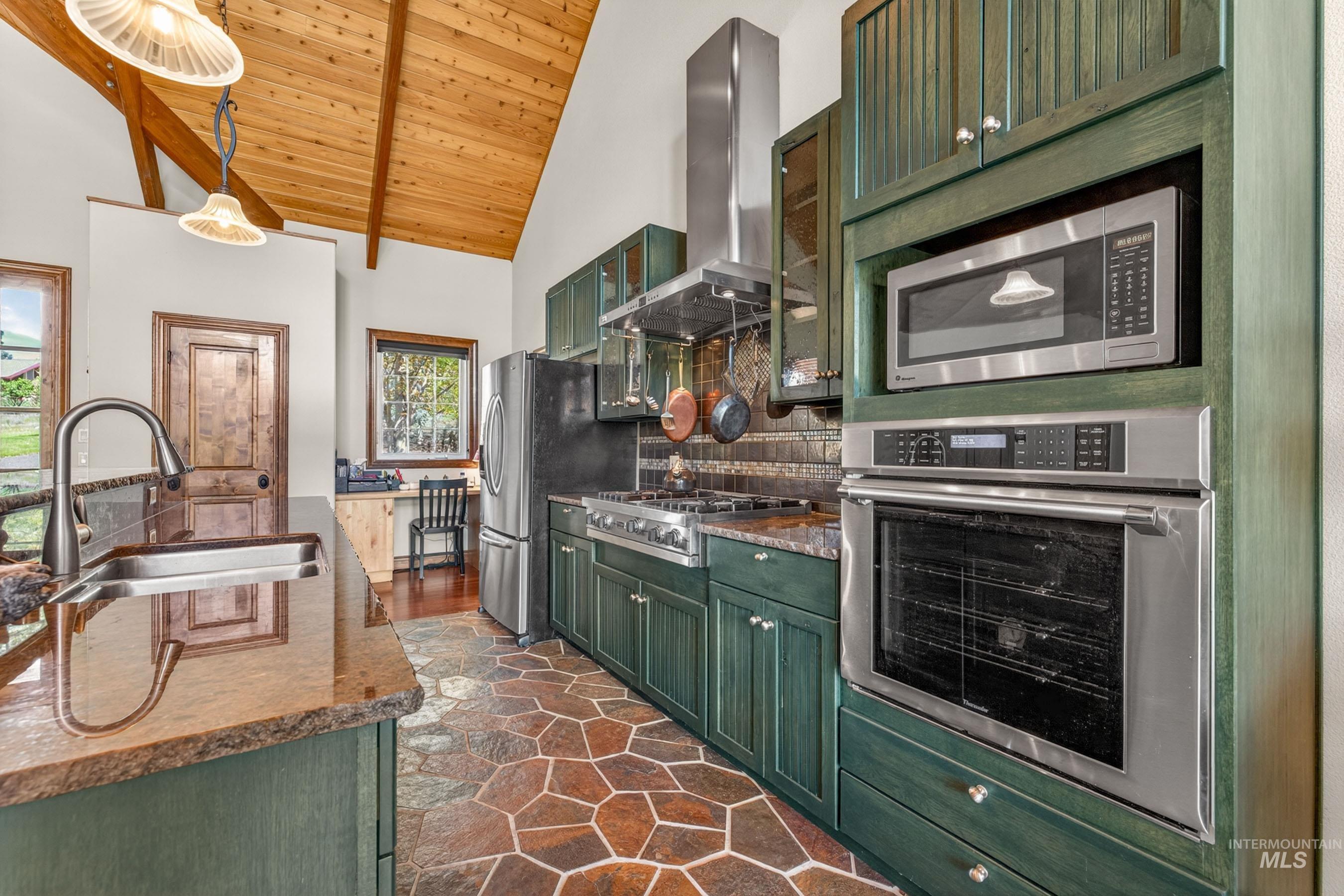 113 Deford Road White Bird, ID 83554 - Photo 11 of 49 Kitchen featuring vaulted wood-paneled ceilings with exposed beams, stone tile flooring, green wood cabinetry, stainless steel appliances, and a built-in desk area
