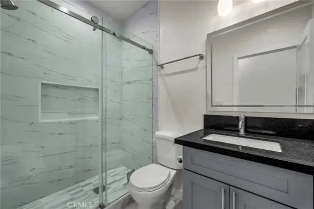 a bathroom with a granite countertop sink a toilet a mirror and shower