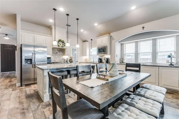 a dining room with stainless steel appliances kitchen island granite countertop a table chairs and a refrigerator