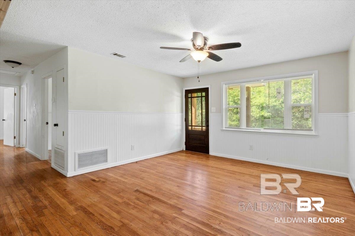 29397 Loper Road Loxley, AL 36551 - Photo 12 of 22 Empty room featuring wood finished floors, a wainscoted wall, a textured ceiling, and a ceiling fan