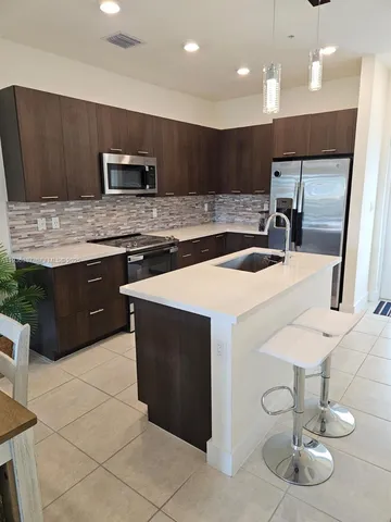 a kitchen with stainless steel appliances a sink a stove a microwave a center island and chairs