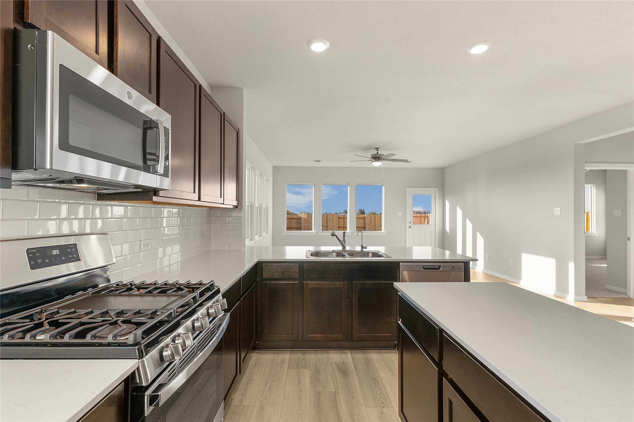 25628 Wheat Seed Lane Elgin, TX 78621 - Photo 2 of 20 Kitchen featuring stainless steel appliances, dark wood finish cabinetry, light wood-style floors, backsplash, and a ceiling fan