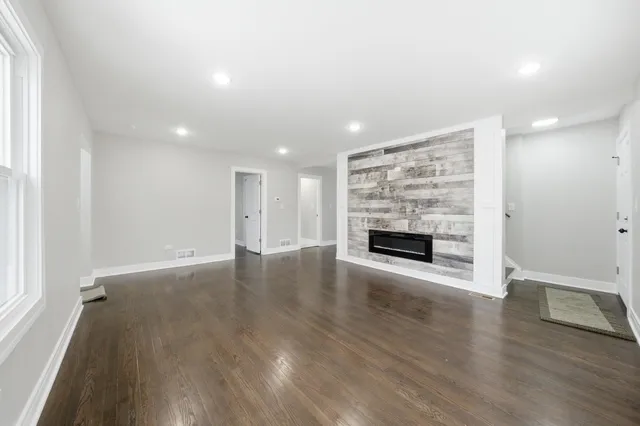 an empty room with wooden floor fireplace and windows