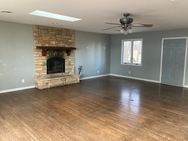 a view of an empty room with wooden floor fireplace and a window