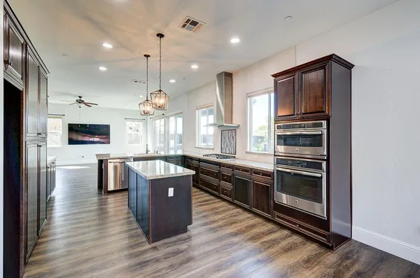 a view of an empty room with wooden floor and a kitchen