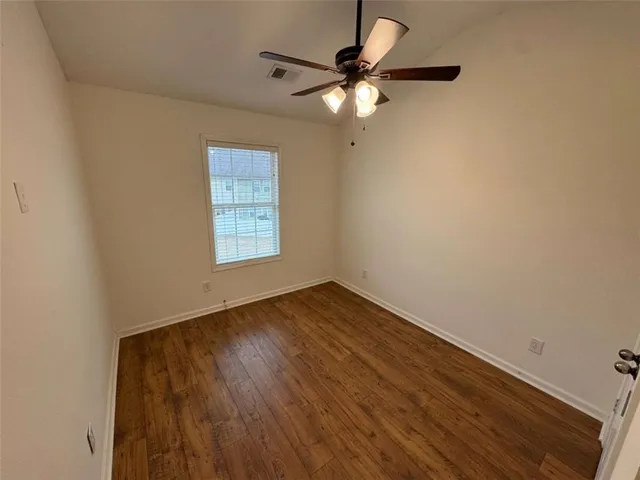 an empty room with wooden floor fan and windows